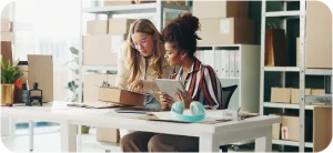 Diverse JVRC logistics team women collaborating with tablet and boxes in modern warehouse for inventory audits