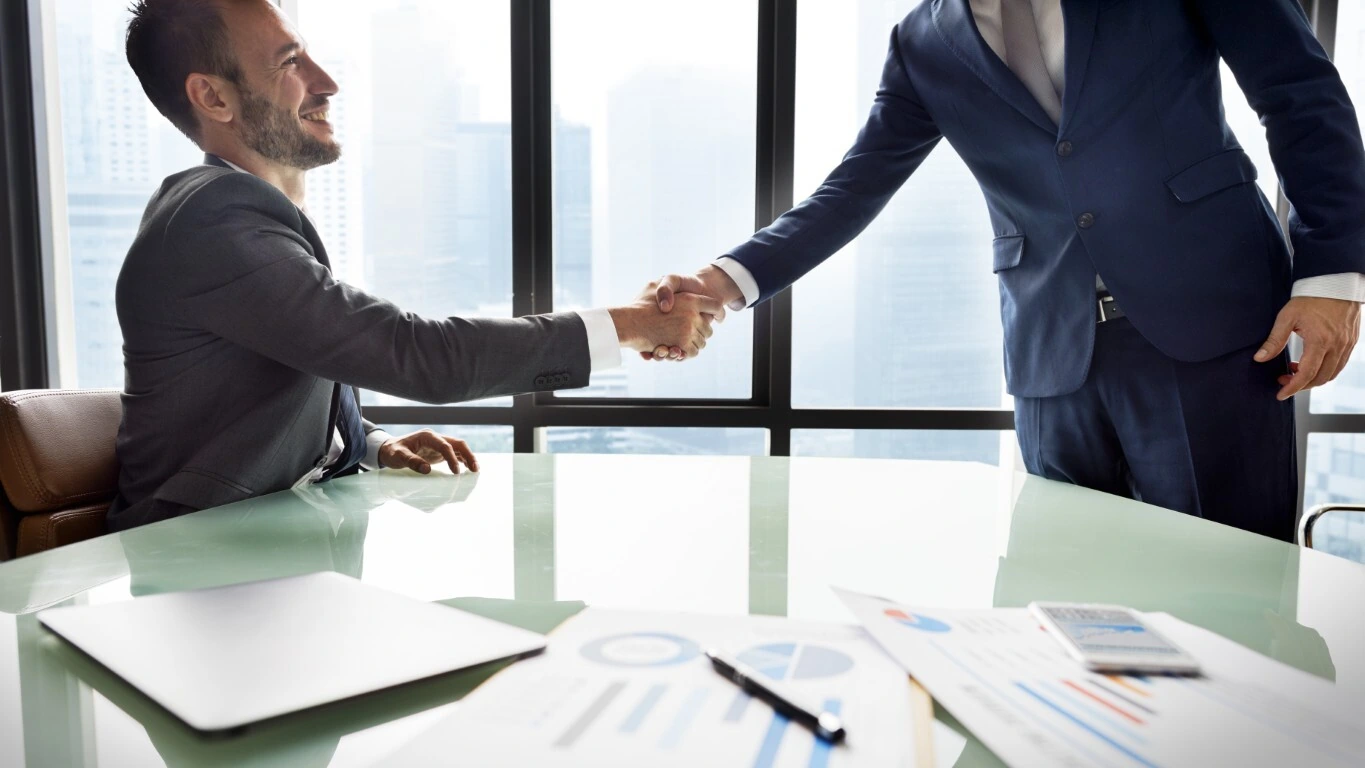 A businessman shakes his insurance rep's hand after renewing his insurance policy.